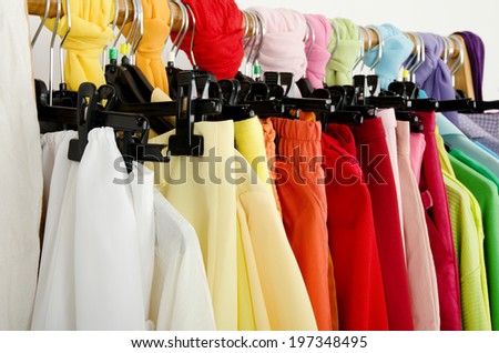 Close up on color coordinated clothes on hangers in a store. Detail on all colors clothes hanging on a rack nicely arranged.