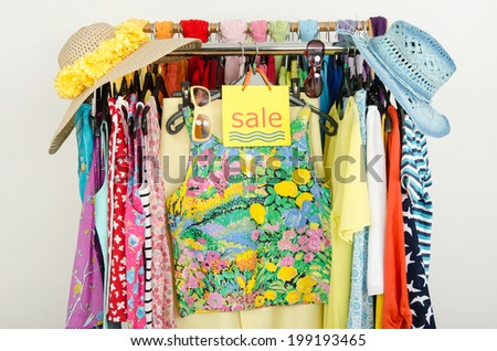 Sale sign for summer clothes. Clearance rack with colorful summer outfits and accessories displayed on hangers.