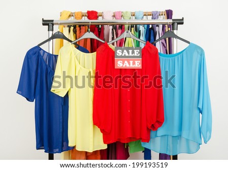 Cute red, yellow, blue blouses displayed on hangers with the sale sign. Rack with colorful summer clothes and accessories on clearance.