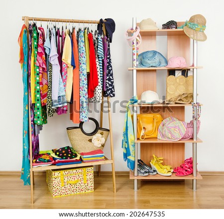 Wardrobe with summer clothes nicely arranged. Dressing closet with colorful clothes and accessories on hangers and a shelf.