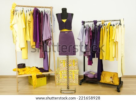Dressing closet with complementary colors violet and yellow clothes. Wardrobe with purple and yellow clothes arranged on hangers and an outfit on a mannequin.
