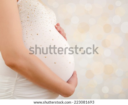 Close up on woman holing her pregnant belly. Woman dressed in white expecting a baby.