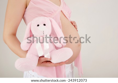 Close up on pregnant belly with toy.Woman expecting a baby with a cute pink rabbit toy in her hand. Easter baby.