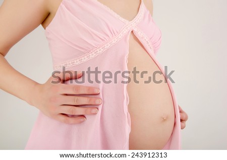 Close up on pregnant belly. Woman expecting a baby dressed in pink lingerie.