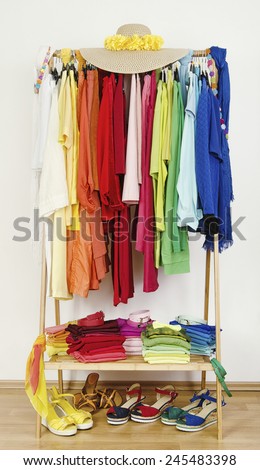 Wardrobe with summer clothes nicely arranged by colors. Dressing closet with color coordinated clothes on hangers, sandals and accessories.
