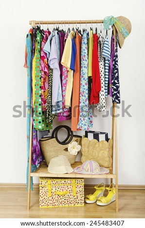 Wardrobe with summer clothes nicely arranged. Dressing closet with colorful clothes and accessories on hangers and a shelf.