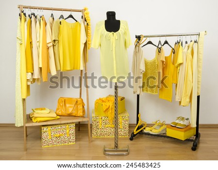 Dressing closet with yellow clothes arranged on hangers and an outfit on a mannequin. Wardrobe full of all shades of yellow clothes, shoes and accessories.
