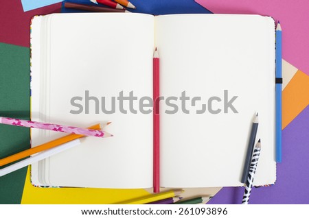 Blank notebook with color pencils. Opened note book on color paper background.