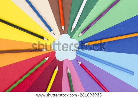 Color pencils on paper with flower memo note. All colors pencils arranged in a circle on rainbow color paper with blank post it note.