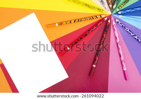 Color pencils and white sheet paper. All colors pencils arranged in a circle on rainbow color paper with blank white paper.
