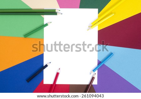 Color pencils and white sheet paper. All colors pencils arranged around a blank white paper with rainbow color paper background.