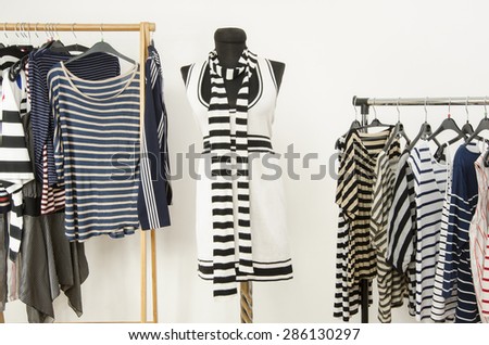 Dressing closet with striped clothes arranged on hangers and a black and white outfit on a mannequin. Colorful wardrobe full of clothes and accessories with stripes pattern.