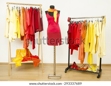 Wardrobe with yellow, orange and red clothes arranged on hangers and a red outfit on a mannequin. Dressing closet with bright color coordinated clothes on hangers, shoes and accessories.