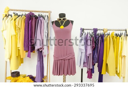 Dressing closet with complementary colors violet and yellow clothes. Wardrobe with purple and yellow clothes arranged on hangers and a summer dress on a mannequin.