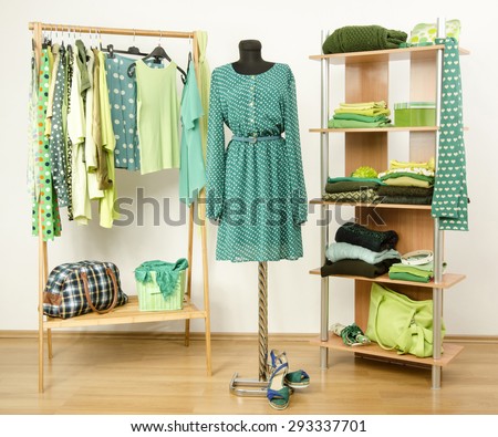 Dressing closet with green clothes arranged on hangers and shelf, dress on a mannequin. Wardrobe full of all shades of green clothes and accessories.