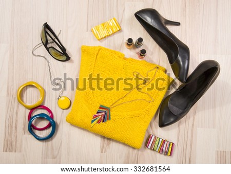 Winter sweater and accessories arranged on the floor. Woman colorful yellow accessories, high heels, sunglasses and nail polish.