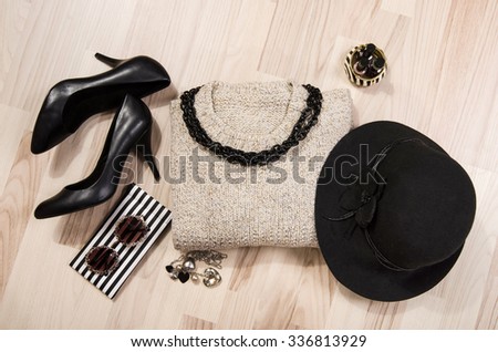 Winter sweater and accessories arranged on the floor. Woman black with silver accessories, high heels, hat, necklace and nail polish.