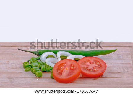 chopped green chillies, sliced tomatoes and sliced onions on aged chopping board and white background. horizontal