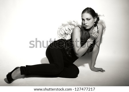 Girl in black with angel wings sitting on the ground and smoke
