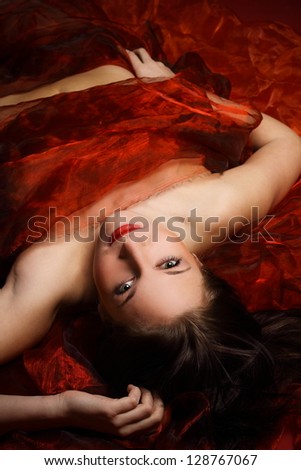 Sexy brunette lying in a red scarves in the studio, intimate places has obscured under scarves
