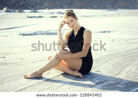 Beautiful blonde in a dress is being photographed in an industrial environment, she sits on the ground, storage environment of fly ash from power plants