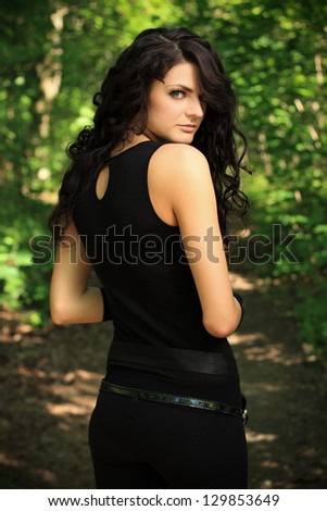 beautiful brunette in a black undershirt, black leggings and the black gloves posing in nature, forest road through the trees, greenery in the background, spring Ã¢Â?Â? May