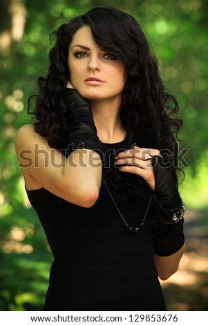 beautiful brunette in a black undershirt, black leggings and the black gloves posing in nature, forest road through the trees, greenery in the background, spring Ã¢Â?Â? May