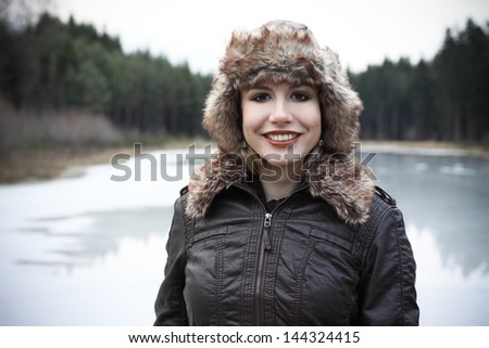 Portrait od beautiful blonde in a leather jacket and fur hat in a nature, next to a pond, fashion photography