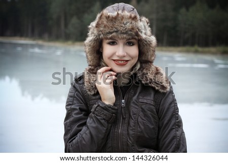 Portrait od beautiful blonde in a leather jacket and fur hat in a nature, next to a pond, fashion photography