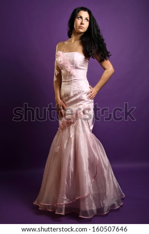 Beautiful brunette in a pink evening dress posing on the purple background, in the studio, fashion photography