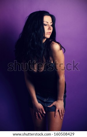 Beautiful brunette in a black shirt and denim skirt posing on the purple background, in the studio, fashion photography