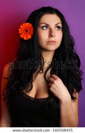Portrait of beautiful brunette in a black shirt, with red flower, on the purple background, in the studio, fashion photography