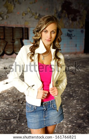 Beautiful brunette in a pink shirt, white jacket and denim skirt posing in a old building, fashion photography