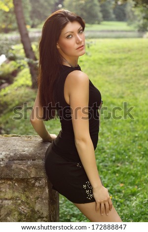 Beautiful brunette in a black shirt and black skirt posing  in a nature, in a park, fashion photography