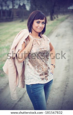 Beautiful brunette in a shirt, jeans and with a blazer posing on a dusty road, in the nature, fashion photography