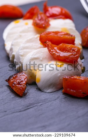 mozzarella with fried tomatos on black stones plates.  caprese salad