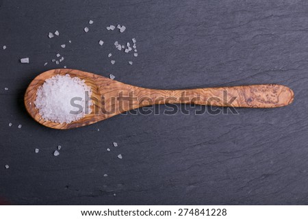 Sea salt in wooden spoon on dark wooden background
