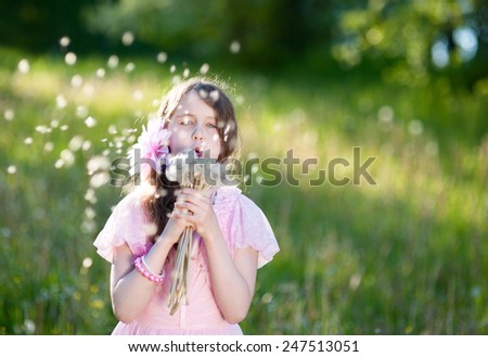The girl in a pink dress blowing a bouquet of dandelions