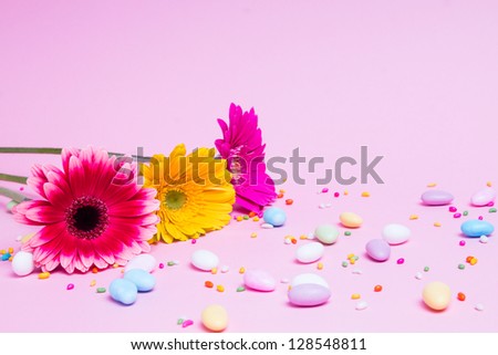 A bouquet of gerberas with small colorful candies. Yellow, red, pink flowers and candies on the pink background.