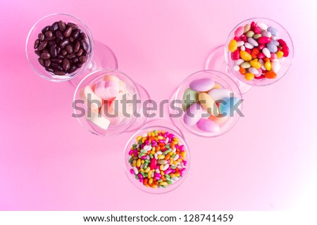 Sweets of bright colors on the pink background. Candy heaps of different sizes in the glass bowls.