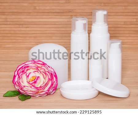 Open jar of cream and other body care cosmetics with a flower on wooden background