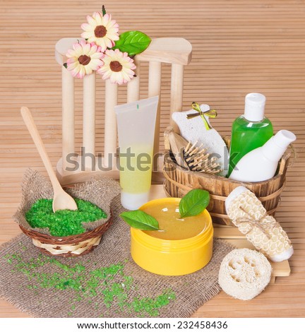 Spa and body care cosmetics and accessories: bath sea salt, natural body scrub, shampoo, shower gel, pumice, wisp, loofah, massage comb with green leaves and flowers on wooden surface