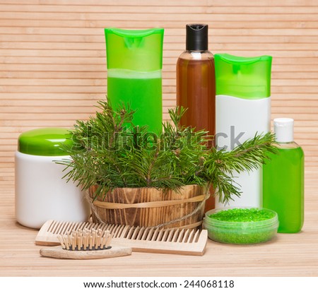 Natural hair care cosmetics and accessories: wooden basket filled with pine branches, sea salt, shampoo, conditioner, balm, mask, wooden combs