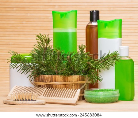 Natural hair care cosmetics and accessories: wooden basket filled with pine branches, sea salt, shampoo, conditioner, balm, mask, wooden combs