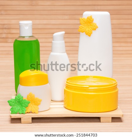 Different cosmetic products for body care: open jar filled with natural scrub, face cream and other cosmetic products on wooden surface. Yellow and green colors