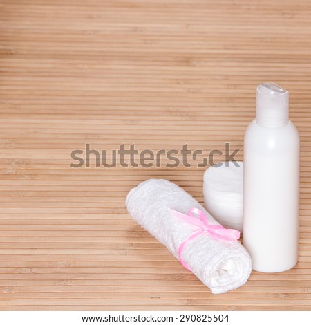 Container of skin cleansing product with a terry towel and cotton pads on wooden surface. Large copy space. Cosmetic theme background
