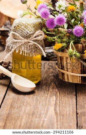 Bottle filled with fresh, raw honey, wooden spoon, bouquet of wildflowers in ligneous basket on wooden planks