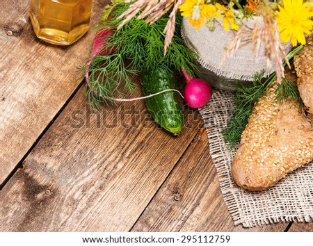 Organic farming food. Freshly baked grain bread with sesame, cucumber, radish, dill, vegetable oil on burlap napkin with bouquet of wild flowers. Wooden planks background. Copy space