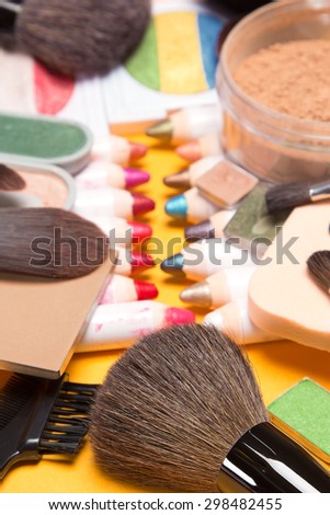 Various makeup cosmetics and accessories: lip liners and eyeliners, loose and compact powder, multicolored eyeshadow, cosmetic sponge and different makeup brushes. Very shallow depth of field