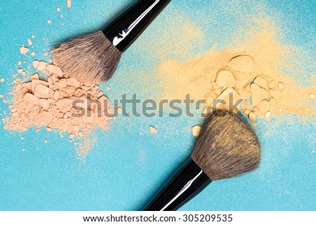 Close-up of crushed mineral matte compact powder and shimmer powder golden color with makeup brushes on blue background